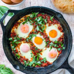 Turkish Shakshuka in a cast iron pan. There are 5 poached eggs in tomato sauce, topped with fresh parsley.