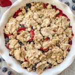 Mixed Berry Cobbler in a white pie dish with blueberries, and strawberries around the dish.