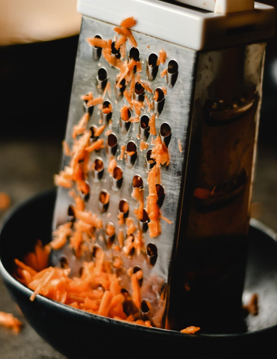 Cheese grater with shredded carrots in it.