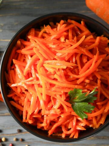 Raw carrot salad in a black bowl topped with parsley.