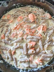 Salmon, mixed in the cream sauce with pasta in a cast iron skillet.