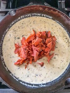 Cream sauce in a cast iron skillet with cooked salmon dropped in the center.