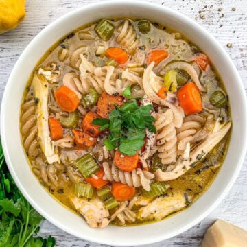 Chicken noodle soup in a white bowl topped with fresh parsley.