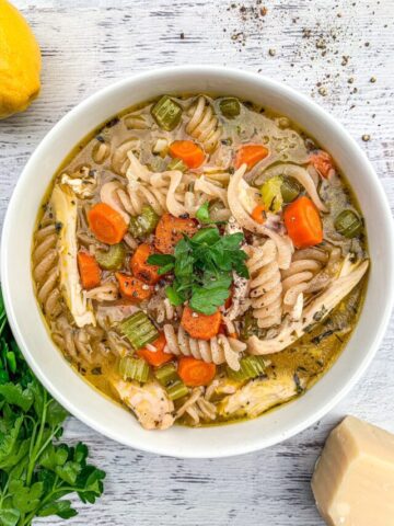 Chicken noodle soup in a white bowl topped with fresh parsley.