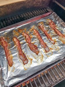 Cooked bacon on a tin foil lined baking sheet on a Traeger Grill.