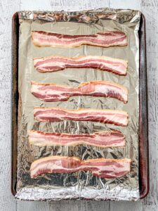 Uncooked Bacon on a sheet pan lined with tin foil.