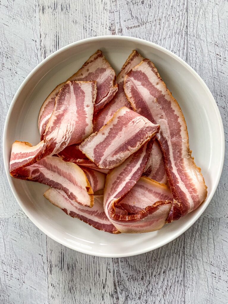 Uncooked bacon on a white plate on a white background.