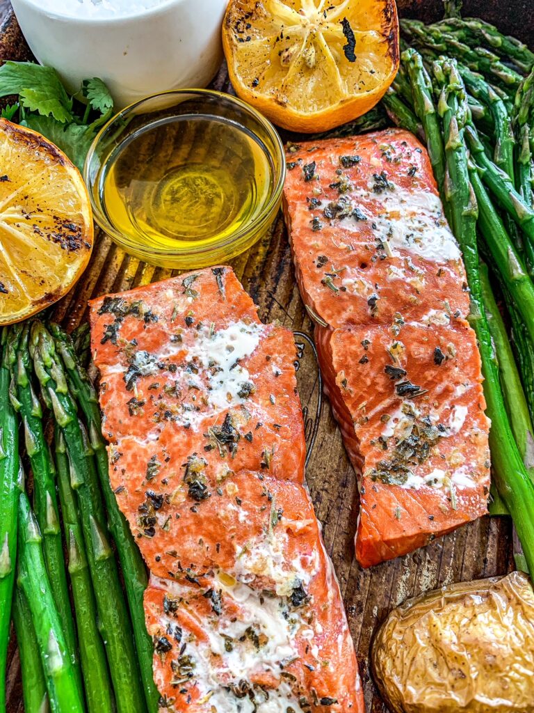 Two grilled salmon filets with asparagus and roasted potatoes on a baking sheet.