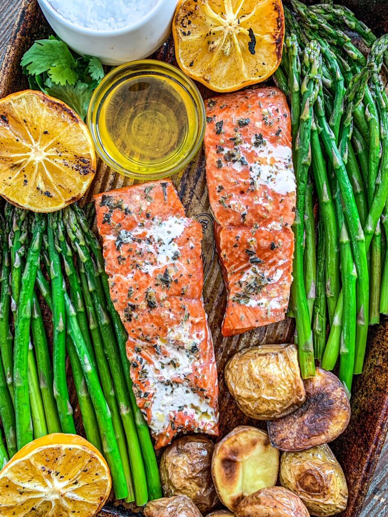 Grilled salmon on a sheet pan surrounded by asparagus, potatoes and grilled lemon.