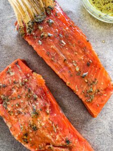 Two salmon filets with one being brushed with an herb butter mixture.