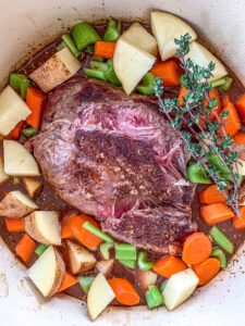 Chuck Roast in a dutch oven along with braising liquid, celery, carrots and herbs.