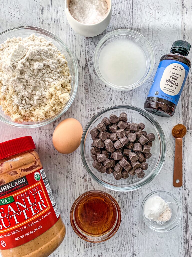 Chocolate chips, almond flour, coconut oil, sea salt, maple syrup and an egg on a table.