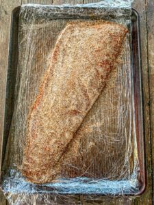 Salmon filet covered with sea salt and coconut sugar on plastic wrap.