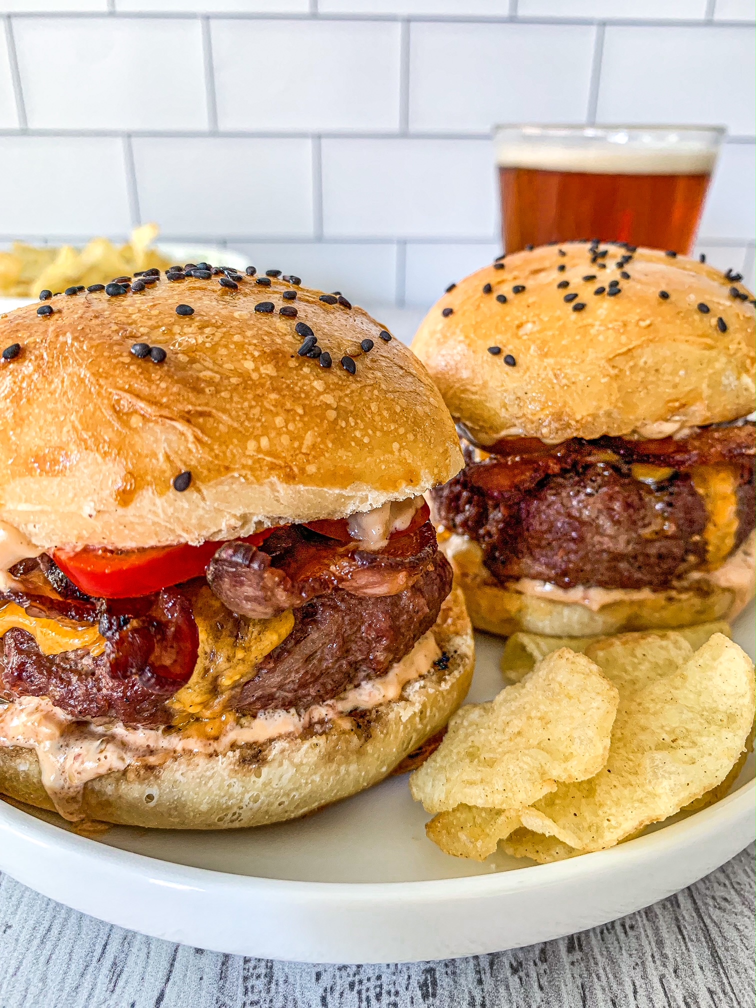 Two Smoked Burgers on hamburger buns with chips and a beer next to them.
