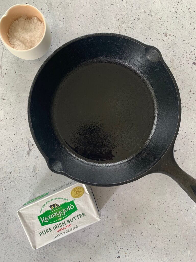 Cast iron skillet, Kerrygold butter and sea salt on a white surface.