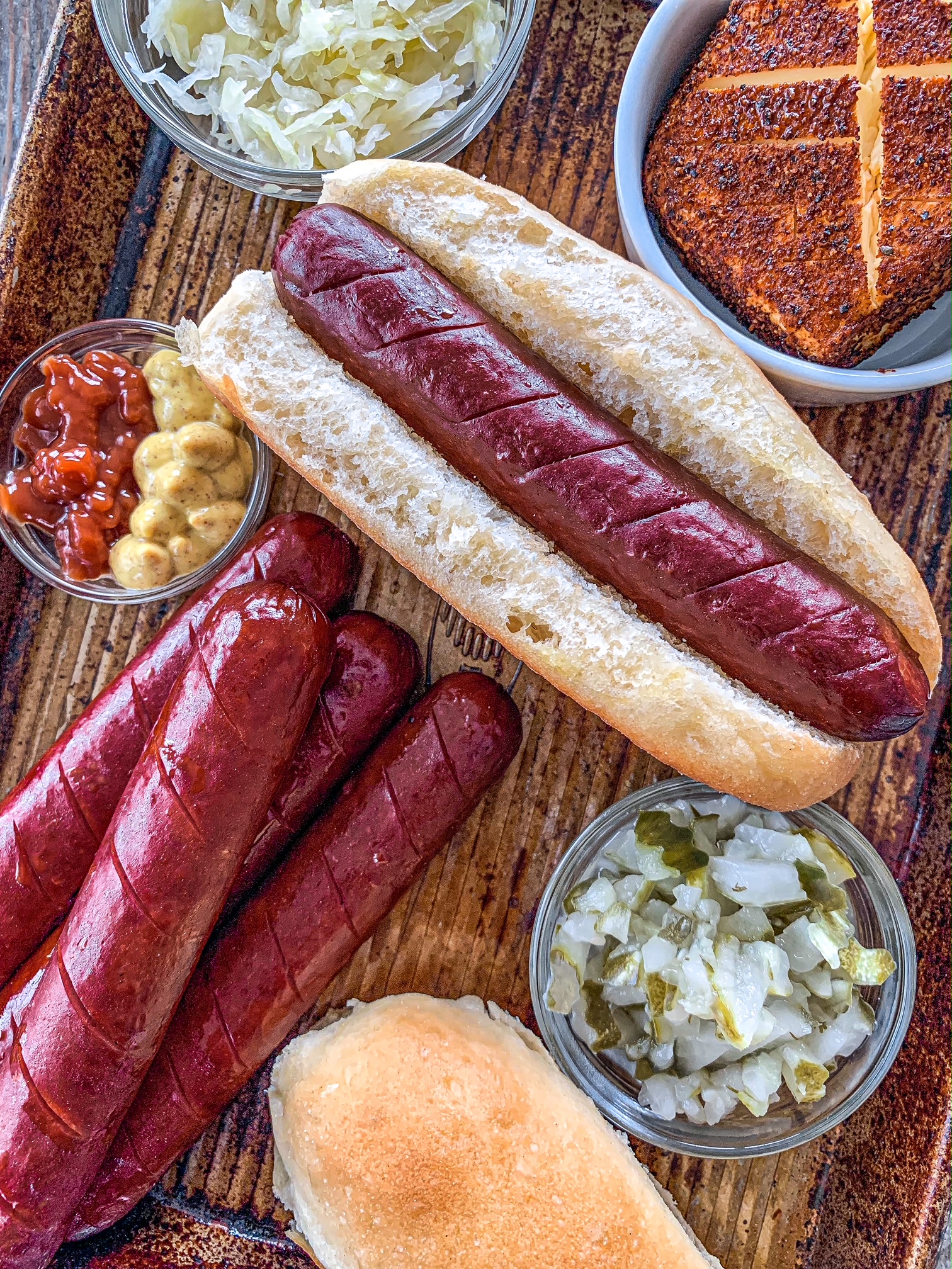 Hot dog on a sheet pan with bowls of smoked cream cheese, relish, ketchup and mustard.