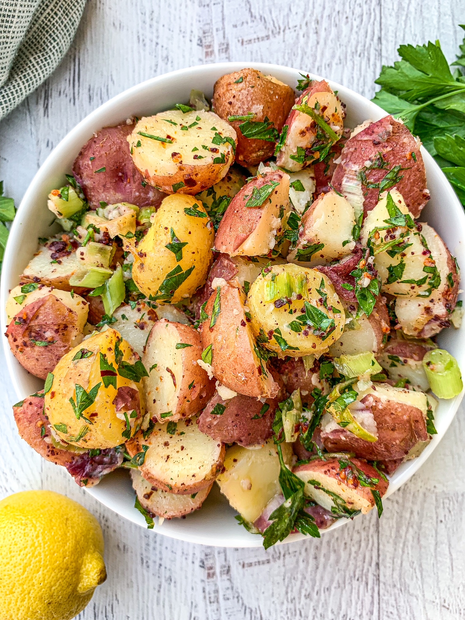 Turkish Potato Salad in a white bowl covered with herbs. Lemon is on the left side with some parsley.