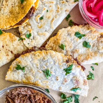 Barbacoa Quesadillas on a sheet of parchment paper with shredded barbacoa in a bowl