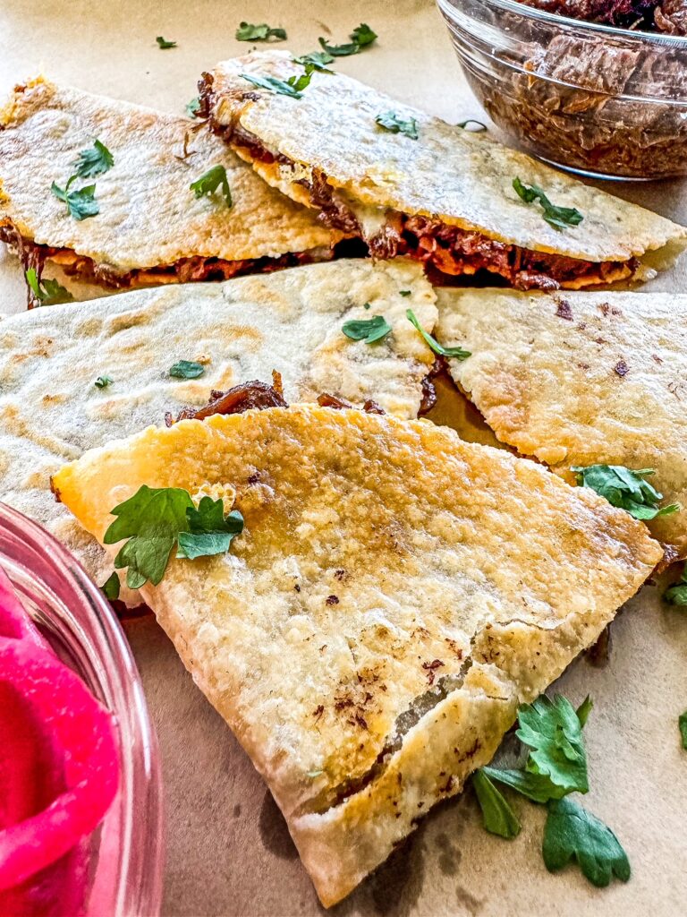 Barbacoa Quesadillas on a sheet of parchment paper with red picked onions.