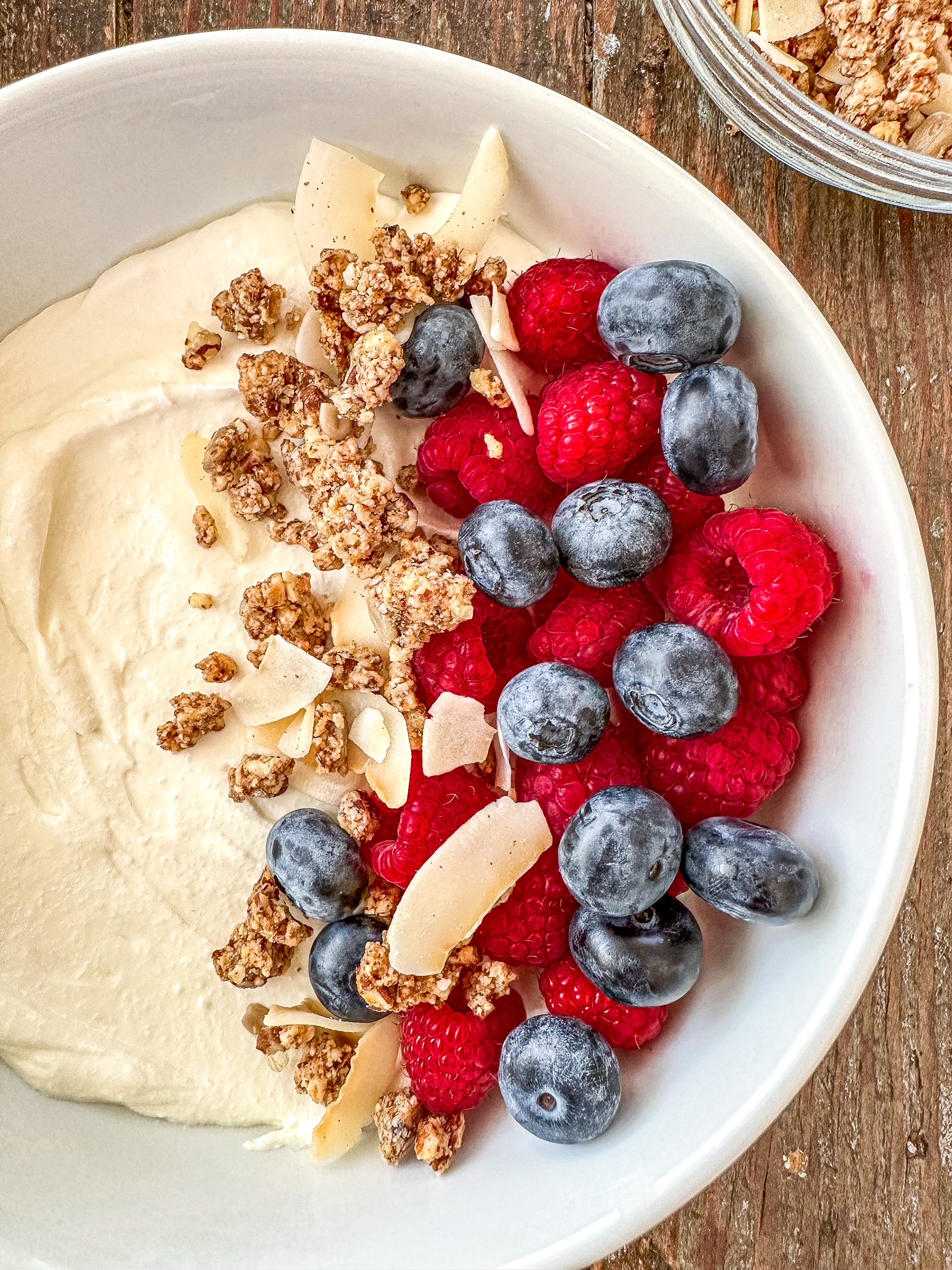 Blended cottage cheese in a white bowl topped with raspberries, blueberries and granola.