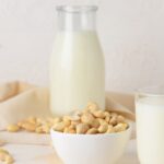 Cashew milk in a glass jar, and cashews in a white bowl.