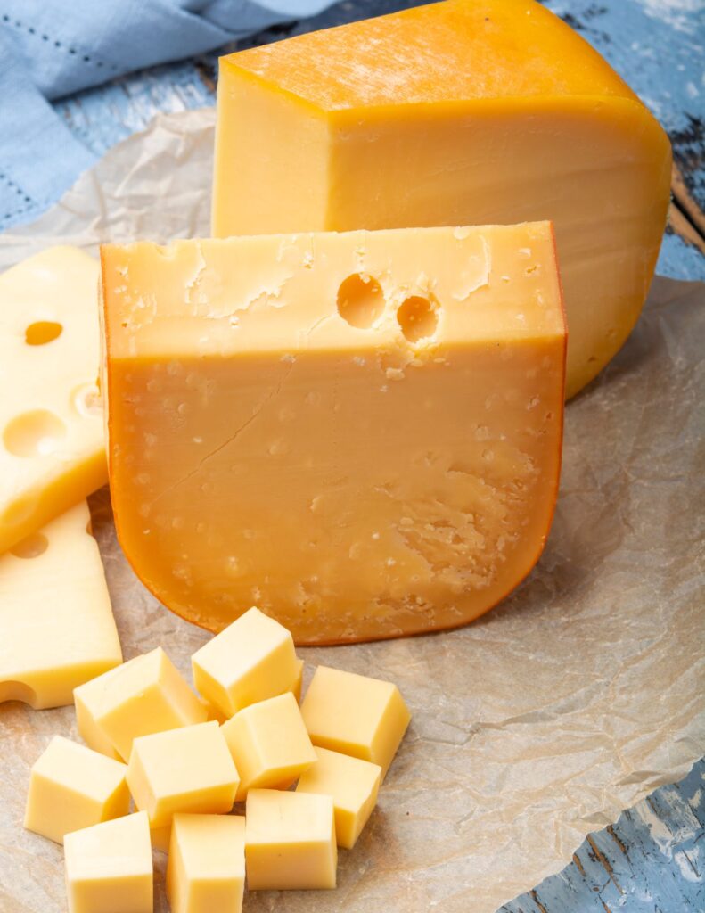 Aged Gouda Cheese in small cubes in the foreground. Two large slices of gouda in the background.