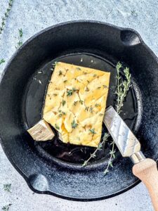 Smoked Feta Cheese in a cast iron skillet with thyme leaves and a cheese knife.