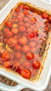 Cherry tomatoes, garlic, and thyme in a white baking dish covered with olive oil.