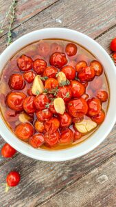Cherry tomatoes, garlic, and thyme in a white bowl on a wood surface.