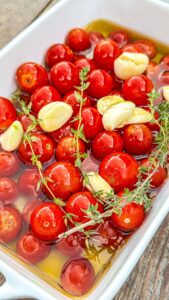Cherry tomatoes, garlic, and thyme in a white baking dish covered with olive oil.