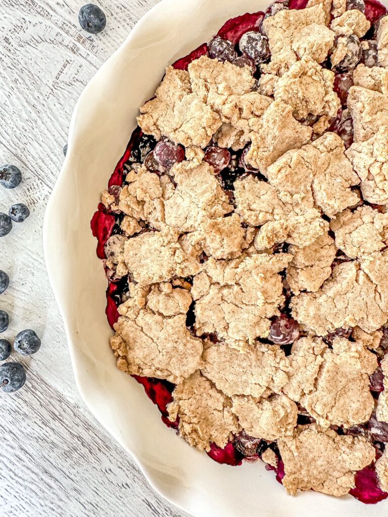 Vegan Blueberry Cobbler in a white pie dish with blueberries off to the side.