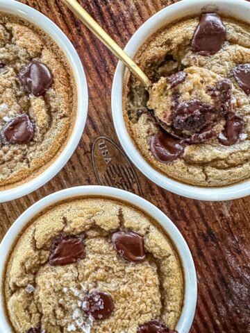 3 single serving white ramekins filled with Cookie Dough Baked Oats. One has a gold spoon coming out of it.