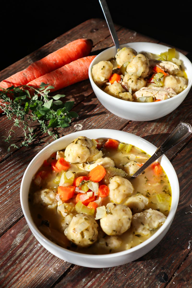 Sourdough chicken and dumplings in a white bowl. Carrots and herbs in the background.