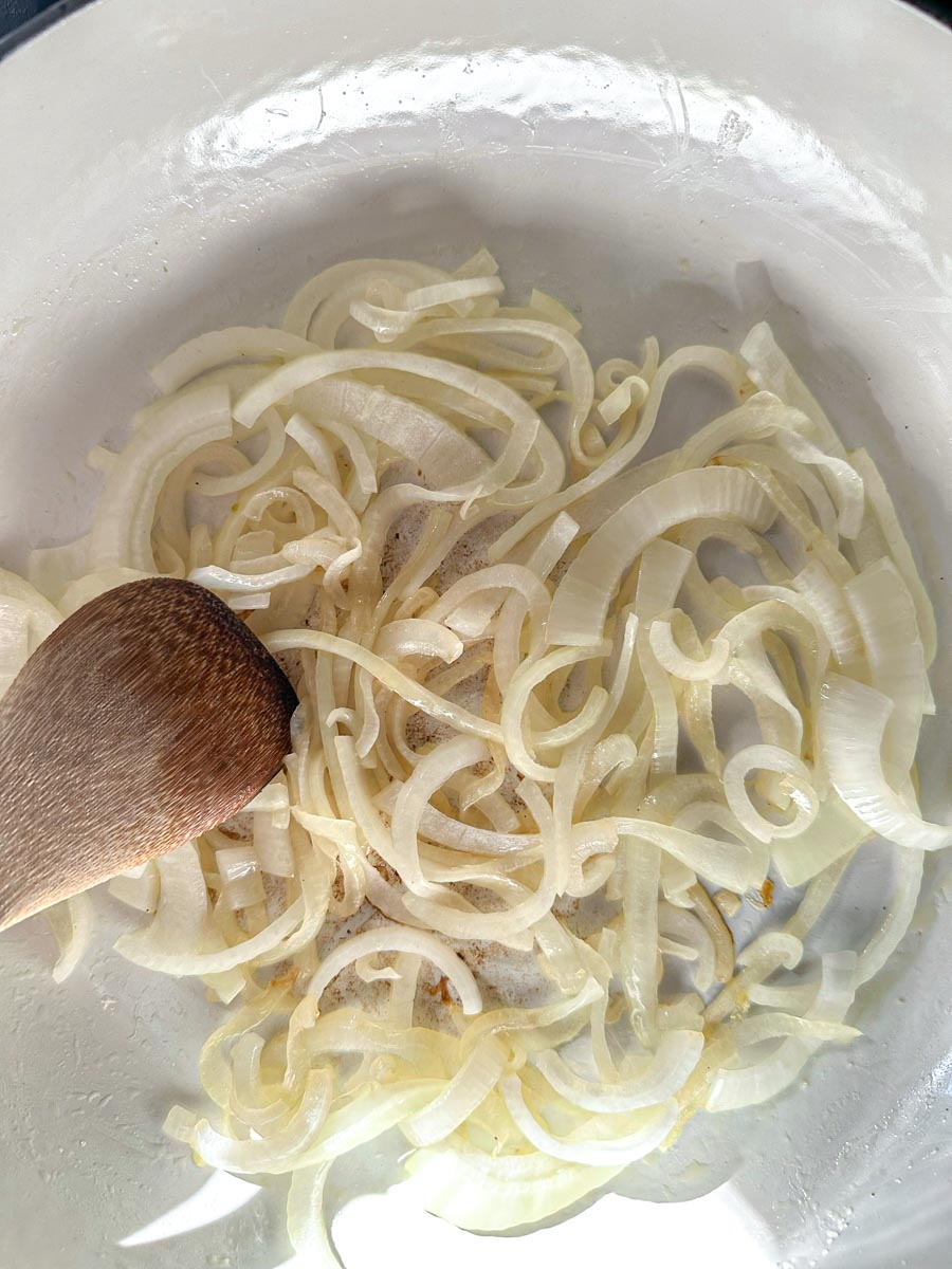 Sautéed onions in a pan with a wooden spoon.