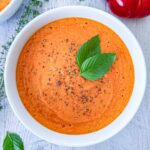 Tomato soup in a white bowl topped with cracked black pepper and basil.