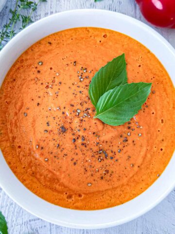 Tomato soup in a white bowl topped with cracked black pepper and basil.