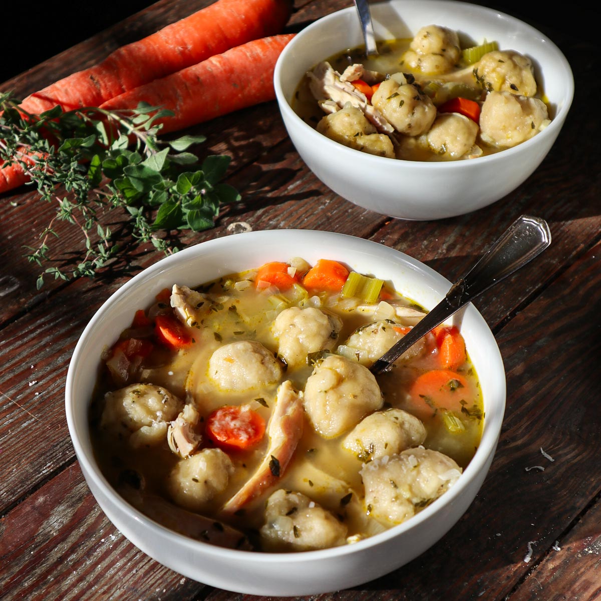 2 bowls full ofSourdough chicken and dumplings. Fresh herbs and carrots in the background.
