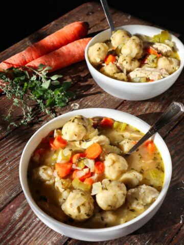 Sourdough chicken and dumplings in a white bowl. Carrots and herbs in the background.