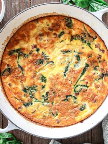 Breakfast casserole in a white braising dish on a wood background.