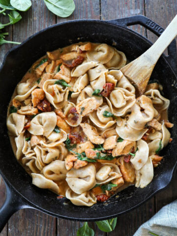 Marry Me Chicken Tortellini in a cast iron skillet with a wooden spoon.