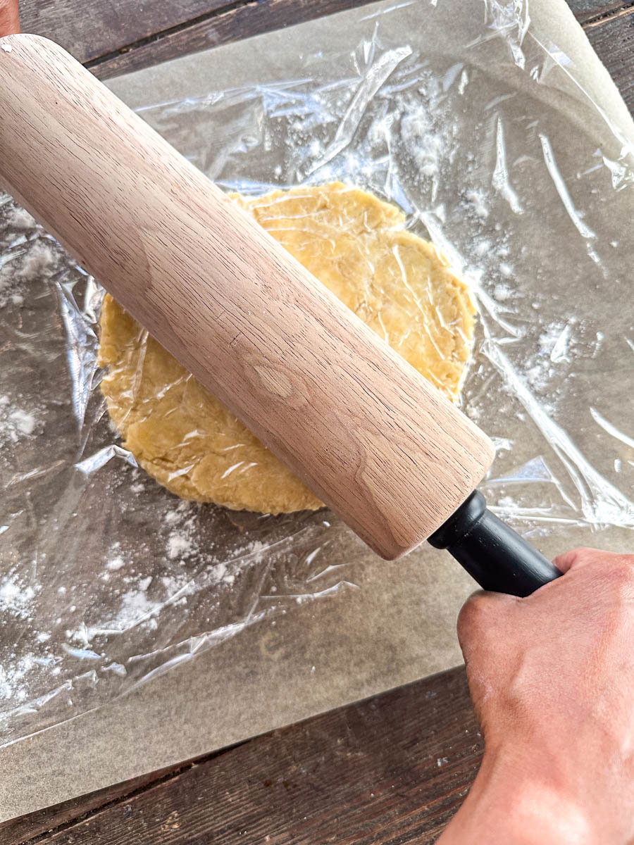 Sourdough pie crust dough on parchment paper being rolled out with rolling pin.