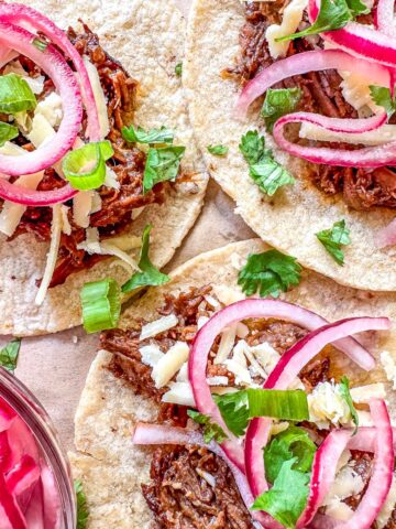3 Tacos de Barbacoa on corn tortillas, topped with white cheddar cheese, pickled red onions and cilantro.