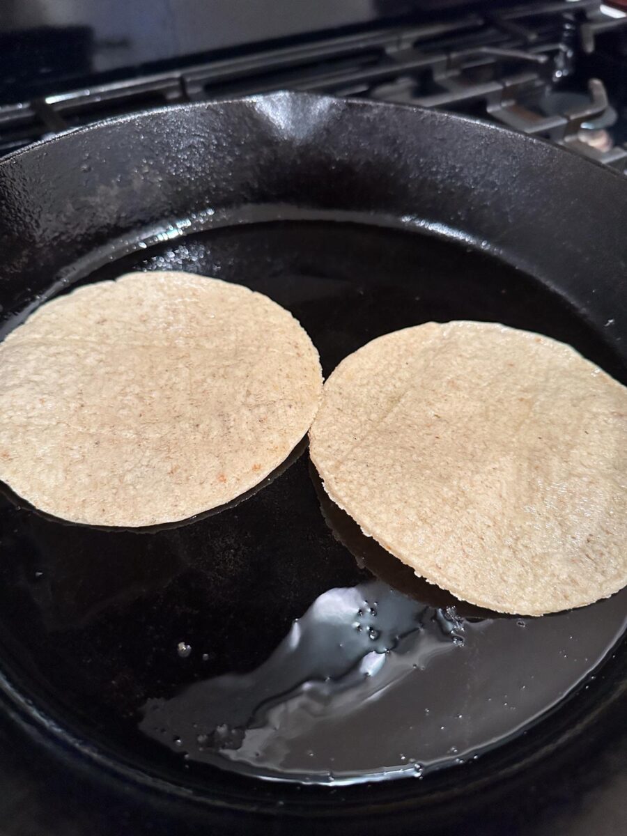 Two corn tortillas in a cast iron skillet.