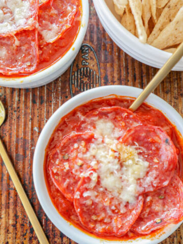 Two cottage cheese pizza bowls topped with parmesan cheese with gold spoons coming out of them.
