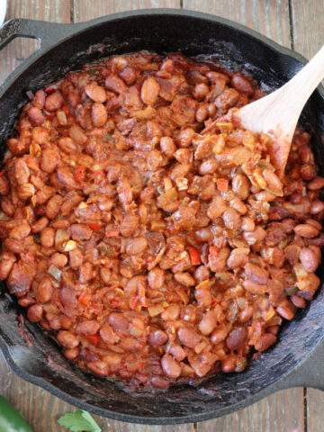 Baked beans in a cast iron skillet with a wooden spoon.