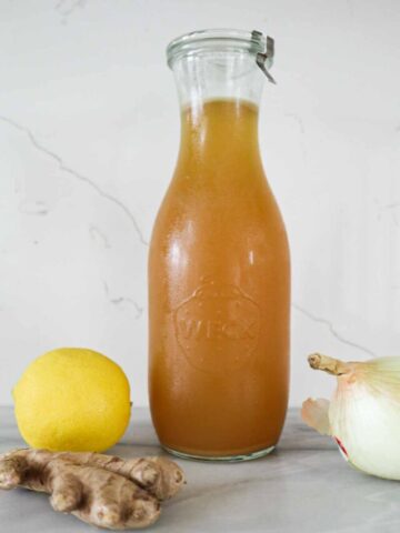 Rotisserie Chicken Bone broth in a large weck jar. Lemon ginger and onion are next to it.