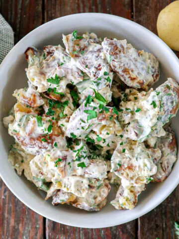Smashed Potato Salad in a white bowl topped with herbs.