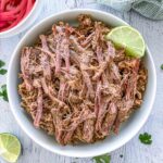 Dutch oven barbacoa in a white bowl with a lime wedge.