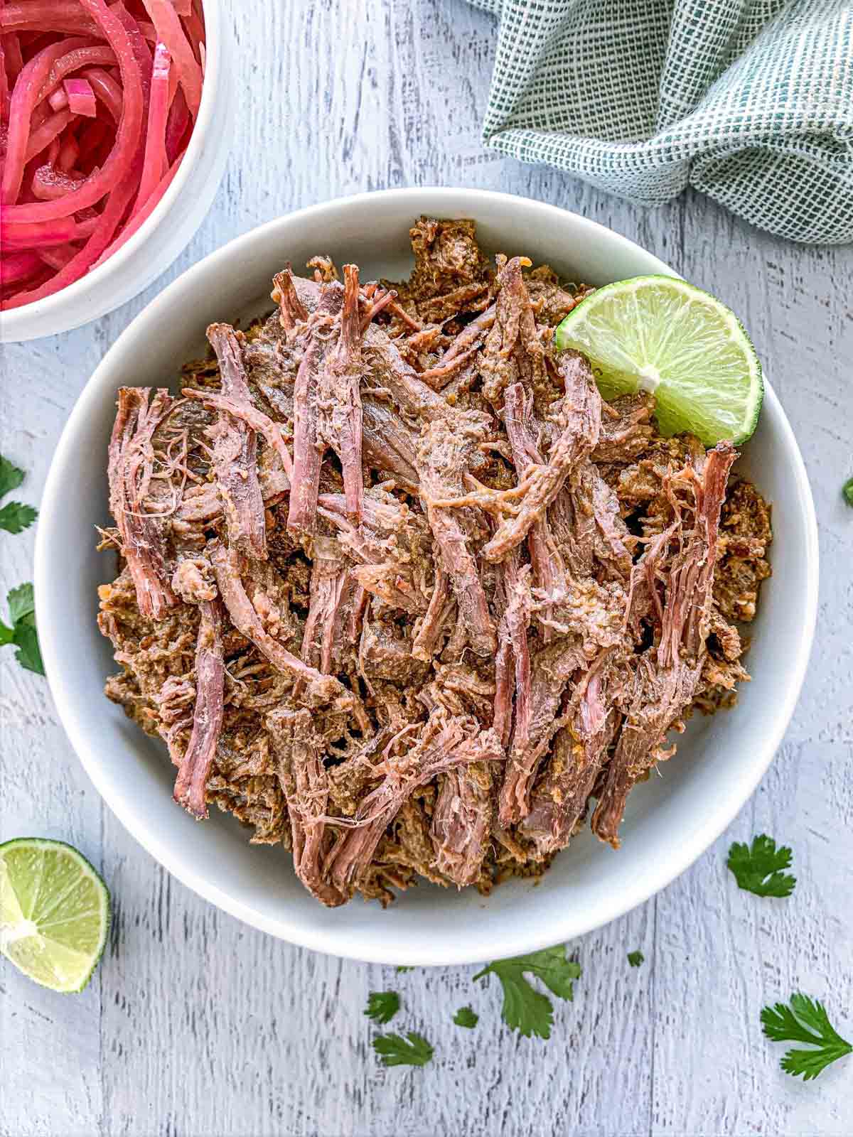 Dutch oven barbacoa in a white bowl with a lime wedge.