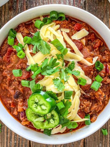 Overhead shot of dutch oven chili topped with white cheddar cheese, green onions cilantro and jalepeno.